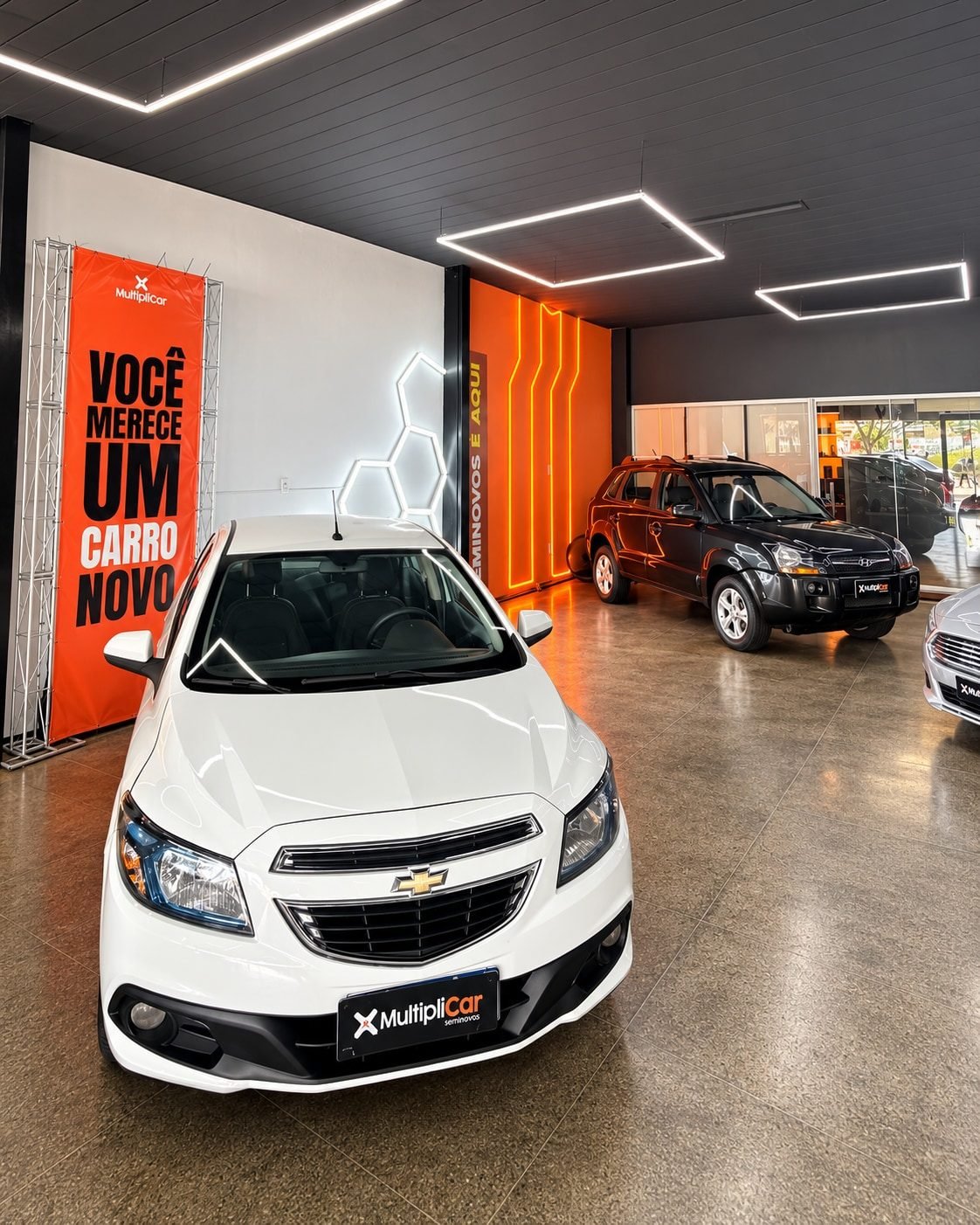 Showroom com Onix branco e banner Você merece um carro novo